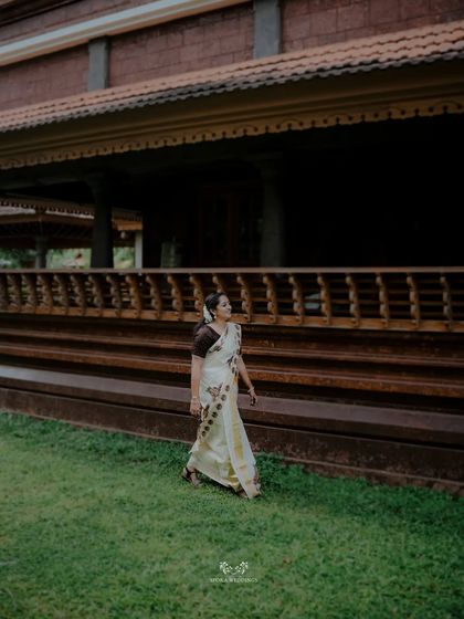 The bride walking gracefully on the lawn of a traditional Kerala building, her simple elegance shining through.