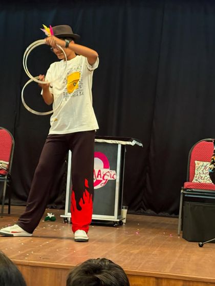 A student confidently performs a magic trick with rings on stage. Our goal is to provide opportunities for kids to discover and showcase their unique talents.