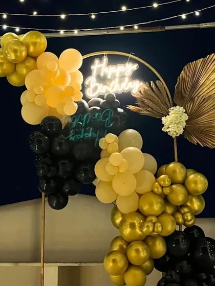A close-up of the black and gold balloon arrangement with a dried palm leaf accent.