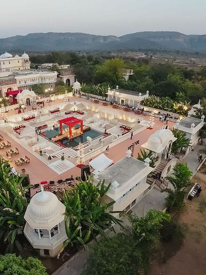 An aerial shot capturing the spectacular scale of the wedding at Alsisar Nahargarh's Hathi Kund. The vibrant red floral mandap sits like a jewel in the water, creating a 360-degree visual spectacle for a truly regal experience.