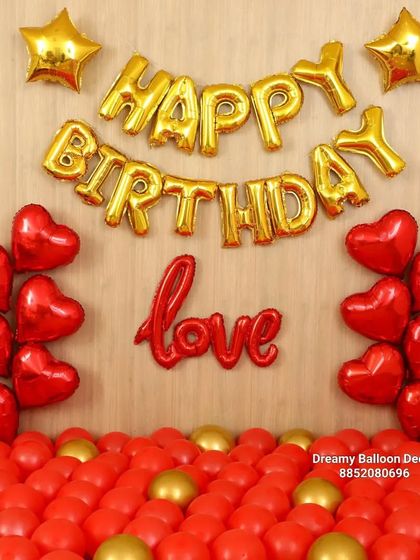 A classic birthday decoration with a romantic twist. This setup features 'Happy Birthday' and 'Love' foil balloons, with red heart-shaped balloons and a floor covered in red and gold balloons.
