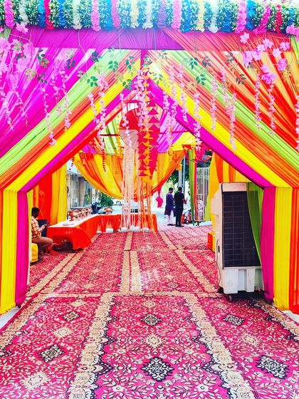 A bright and cheerful tent entrance, decorated with neon-coloured drapes and hanging flowers, perfect for a daytime celebration.
