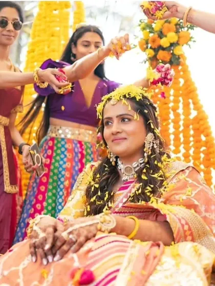 A candid shot from a vibrant Haldi ceremony. The bride's makeup is minimal and fresh, designed to withstand the festivities while letting her natural glow shine through as she's showered with flowers and blessings.