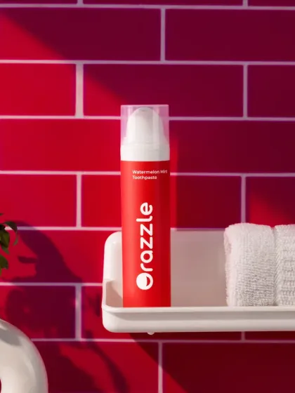 A bathroom shelfie shot for a watermelon-flavored toothpaste. The bold red tile background and simple styling put the focus squarely on the product, showing how it can brighten up a daily routine.