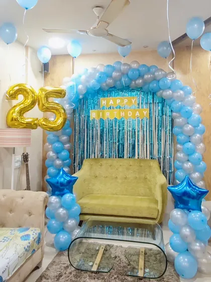 A 25th birthday setup with a blue and silver balloon arch. This decoration transforms a living room space with a shimmer curtain and a large '25' foil balloon, perfect for milestone celebrations.