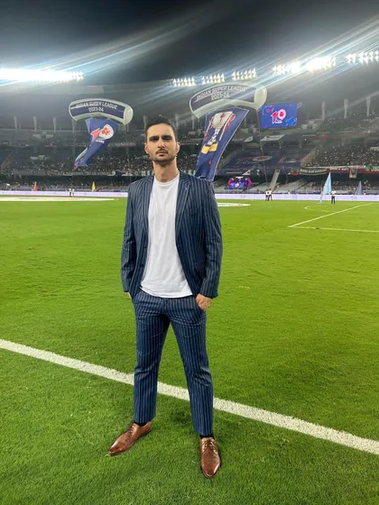 Presenter Karan Sawhney styled for the Indian Super League broadcast. This modern pinstripe suit paired with a simple white tee creates a look that is sharp, professional, and perfect for live television.