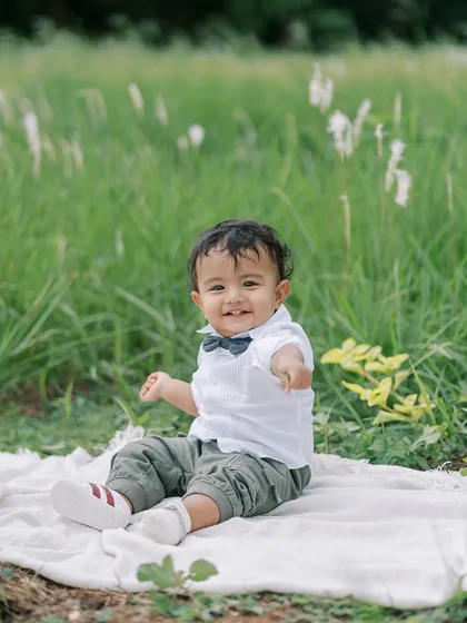 A happy baby boy sitting on a blanket in a field of green. The simple, natural setting allows his joyful personality to be the focus.