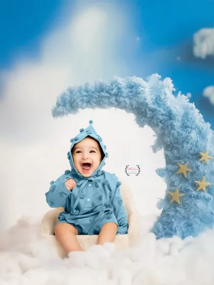 A baby boy dressed in blue laughs with pure delight while sitting on a fluffy, moon-shaped prop. This dreamy, celestial-themed sitter session is perfect for capturing the magic of infancy.