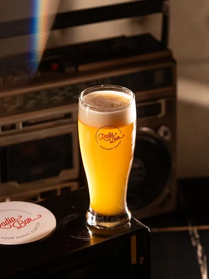 A tall glass of craft beer with a perfect head of foam. The retro boombox in the background helps set the fun, casual vibe of the bar.