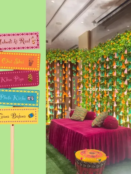 A vibrant Mehndi seating area with a lush green backdrop and fun, quirky signboards for photo ops.