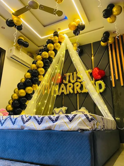 I designed this elegant 'Just Married' room decoration for a newlywed couple. The setup features a stylish black and gold balloon arch over the bed, a fairy light canopy, and large foil letters on the wall. It’s a perfect welcome surprise.