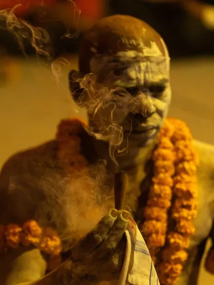 A Naga sadhu, his body covered in ash, is enveloped in a cloud of smoke from his chillum. The image is mystical and captures the otherworldly aura of the ascetics.