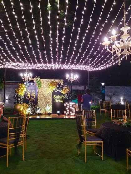 This outdoor 35th birthday party was transformed into an elegant evening affair with a canopy of warm string lights and classic chandeliers. The stage featured a personalized backdrop with marquee numbers, creating a sophisticated atmosphere for a large-scale celebration.