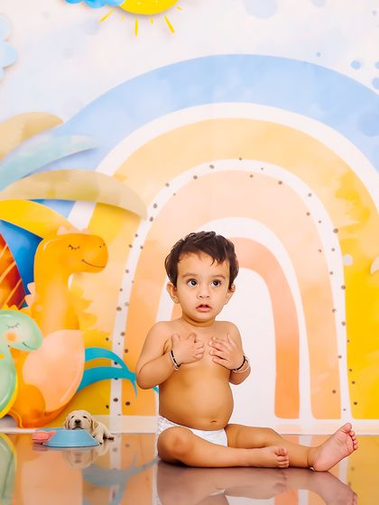 A curious expression from a baby boy in a diaper, set against a colorful dinosaur and rainbow background. This is a simple, sweet shot from a themed sitter session.