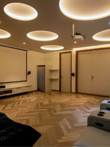A modern and bright home theater with comfortable recliners, herringbone wood flooring, and a unique ceiling design with circular light coves. This space is designed for a fun and relaxed viewing experience.