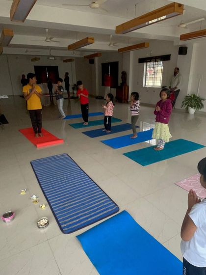 A regular weekly class in session. Children learn the foundations of yoga, including standing poses and prayer, in a group setting that fosters mutual respect and shared learning.