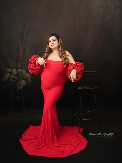 A bold and confident pose in a striking red gown. The unique rose-petal sleeves and the simple, dark background make this a powerful and modern maternity portrait.