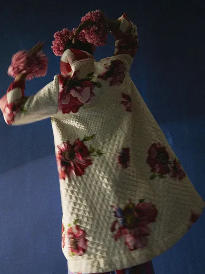 This image showcases the back of a reversible floral jacket, styled with a dramatic floral headpiece. The pose and dark, moody lighting create a sense of mystery and highlight the garment's unique, artistic details.