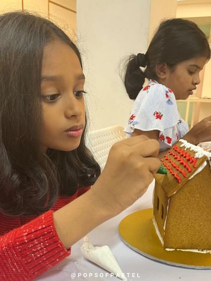 Another young artist meticulously decorates her gingerbread house roof with red icing.