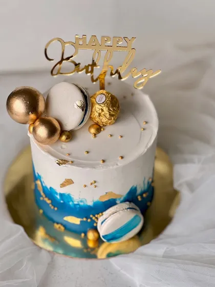 A stylish and masculine design perfect for him. This rich vanilla buttercream cake features a blue watercolor effect, gold leaf, macarons, and a Ferrero Rocher topper.