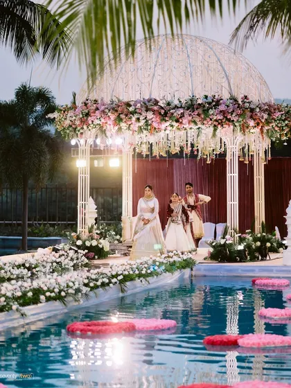 The bride and groom make their entrance onto the poolside mandap at their Karjat wedding, a truly grand and unique setting for their vows.