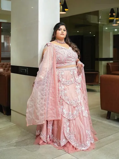 A stunning full-length photo of the bride at her engagement, wearing a beautiful pink layered lehenga.