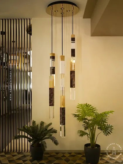 This cluster of pendant lights showcases a luxurious blend of materials, combining solid marble, fluted gold metal, and clear crystal. Suspended at varying heights, they create a dynamic and elegant focal point, ideal for stairwells or entryways.