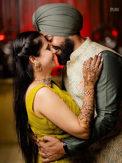 An intimate close-up of the couple during their Mehndi celebration. The bride's intricate henna design with the groom's initial is a beautiful detail.