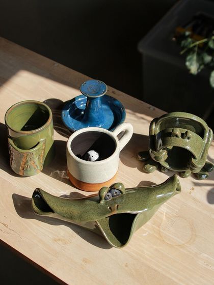 A fun and quirky set of creations, including a crocodile ashtray and a mug with a tiny panda peeking out from inside.