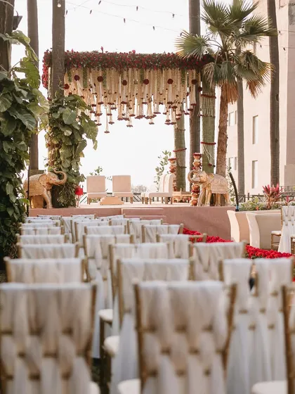 A grand traditional mandap at the Taj Lands End, flanked by statues of elephants and featuring a canopy of red and white florals.