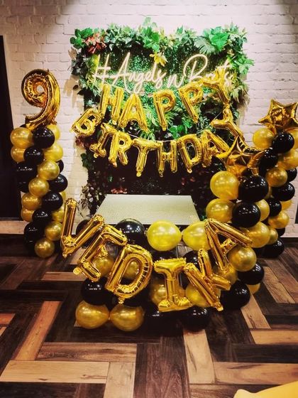 A compact and elegant birthday setup against a greenery wall. I used gold and black balloons to create two pillars and arranged 'HAPPY BIRTHDAY' and the name 'VIDHI' in gold foil balloons.