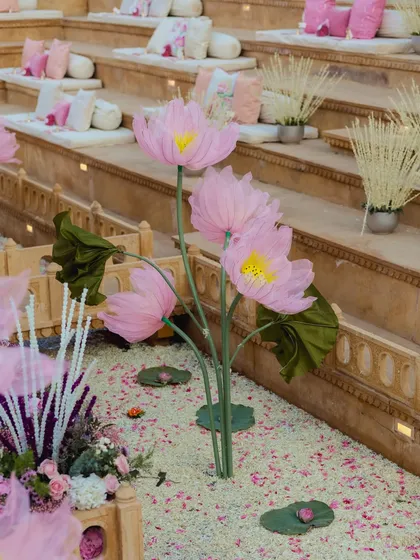 Whimsical, oversized pink lotus flowers stand in a bed of petals, adding a touch of fantasy and artistry to the sacred wedding space.
