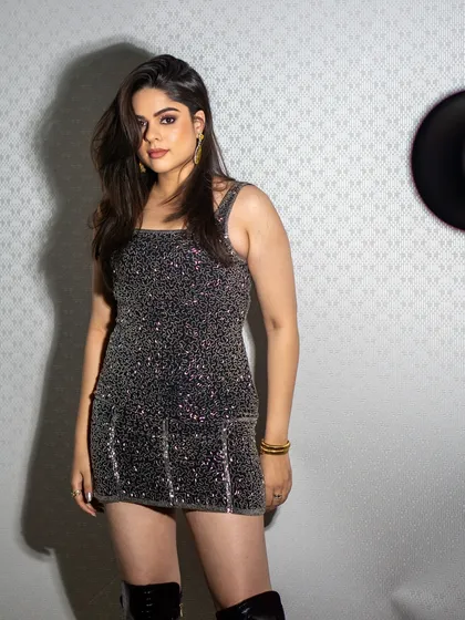 A more casual, on-set style shot of a model in a silver sequined mini dress and thigh-high boots. This look is perfect for a party collection lookbook, feeling both candid and cool.