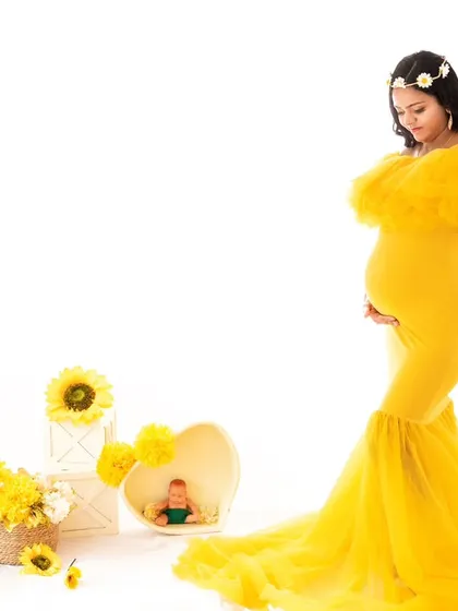 Another pose from the sunny yellow gown session. The mom-to-be stands, holding her bump, offering a full-length view of the beautiful gown and the bright, cheerful studio setup.