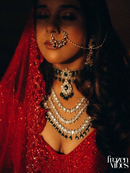 A dramatic, low-key portrait of the bride in her red veil. The focused light on her face and jewelry creates a powerful and cinematic image.