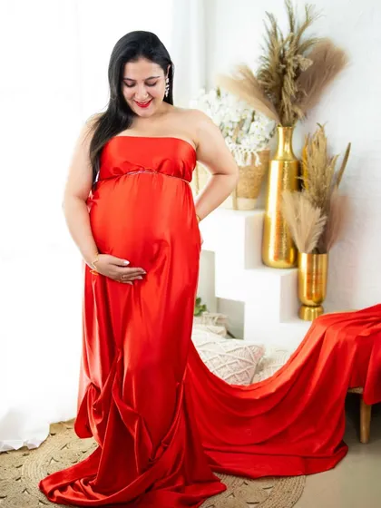A simple yet stunning red satin gown with a long train. This shot, taken in our bright studio, highlights the sleek fabric and the beautiful silhouette of pregnancy.