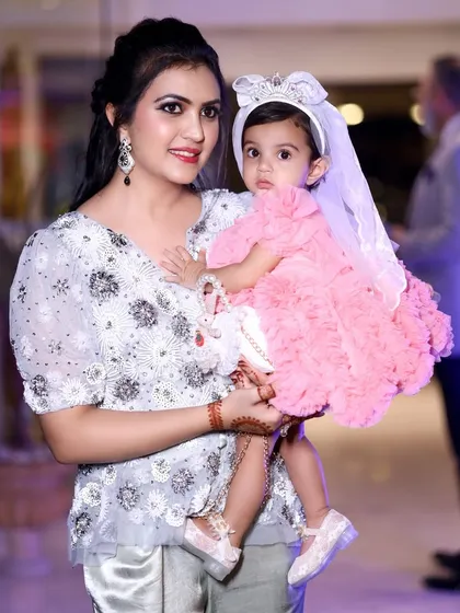 A mother holds her daughter, both posing elegantly for the camera. This portrait highlights their coordinated outfits and the mother's beautiful henna design.