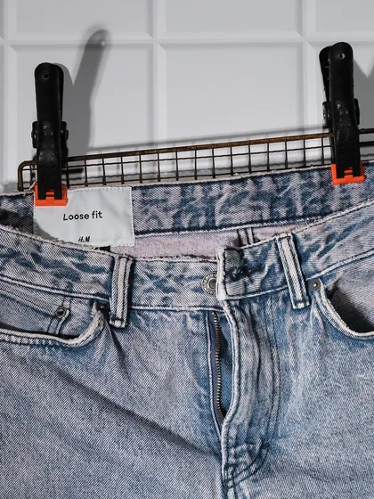 A close-up detail shot of H&M loose-fit jeans, showing the texture, wash, and brand label. Detail shots are crucial for helping customers make purchase decisions.
