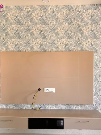 An accent wall can redefine a living space. Here, I installed a subtle botanical leaf pattern wallpaper behind a TV unit, adding a touch of modern elegance and texture that complements the room's neutral furniture.
