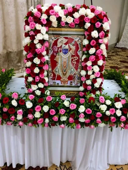 A beautiful floral frame for a Shrinathji portrait, made with red and white roses. This type of arrangement is perfect for creating a focal point for devotion during religious gatherings at home.