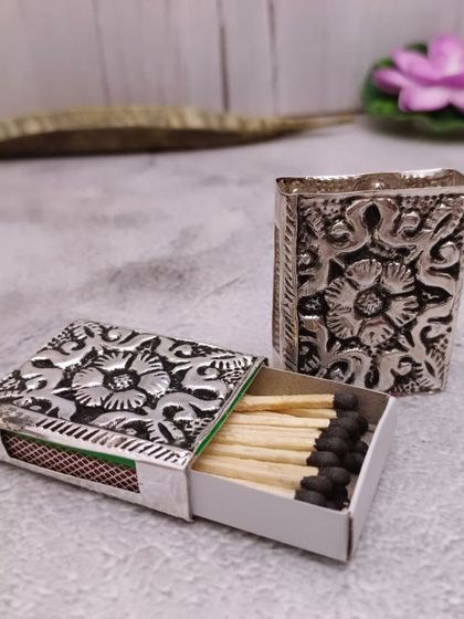A beautifully carved German silver matchbox cover. It's a small detail that adds a lot of elegance to your pooja setup.