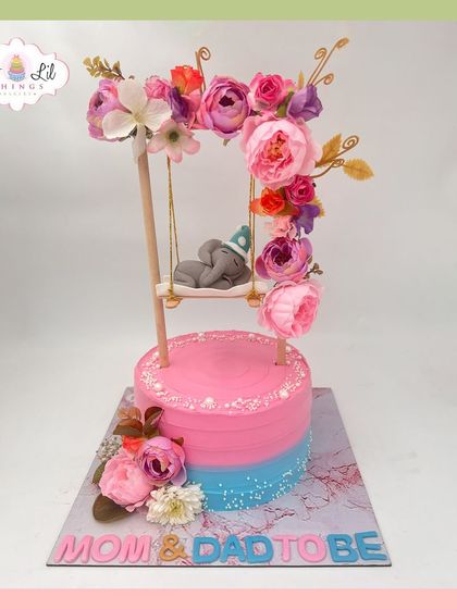 A sweet "Mom & Dad to be" cake, featuring a fondant elephant sleeping on a floral swing.