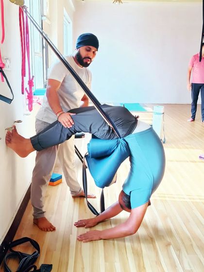 I am assisting a student in a scorpion pose variation using the wall ropes. This setup provides security while he works on his flexibility and strength.