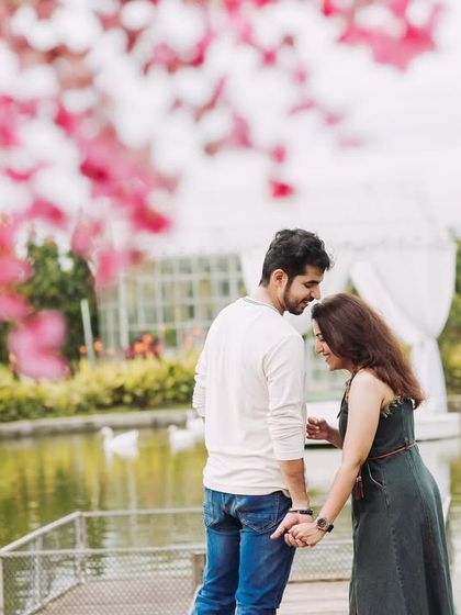 A romantic moment by a pond, framed by beautiful pink blossoms. This composition uses foreground elements to create a soft, dreamy, and intimate portrait.