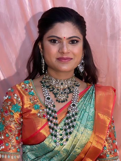 Bride Swathi's reception look is all about regal elegance. She wears a beautiful sea green and orange saree, paired with a stunning multi-layered emerald necklace.