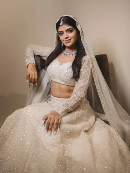 A graceful portrait of the bride, Prachi, seated in her stunning white engagement lehenga. Her elegant pose and the soft lighting create a timeless look.