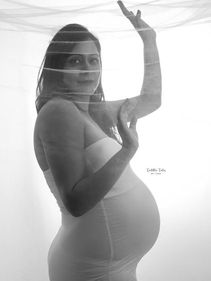 A dance of light and shadow. This artistic black and white portrait uses a sheer veil to create a mysterious and ethereal effect, highlighting the silhouette of the mother-to-be.