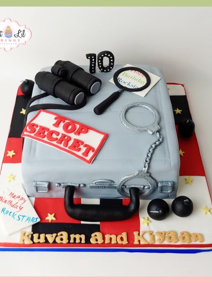 Mission: Birthday! This "Top Secret" spy-themed cake is perfect for a joint 10th birthday. Shaped like a briefcase, it's adorned with edible handcuffs, binoculars, and a magnifying glass for a mysterious and fun party.