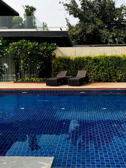 The deep blue tiles of the pool contrast beautifully with the warm wood of the deck and the vibrant green of the surrounding hedge.