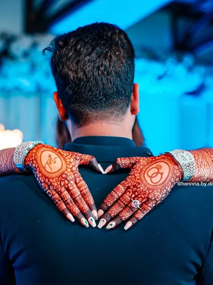 Capturing the beautiful moments after the mehendi is applied is just as important. Here, the bride's hands, adorned with personalized henna featuring the couple's initials, form a heart around her partner, showcasing the rich, dark stain.